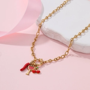 Goldene Halskette mit Kirschen-, Chili- und Cocktail-Anhängern auf rosa Hintergrund