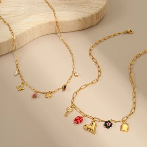 Collares dorados con colgantes de corazón, perlas y dijes sobre fondo de mármol