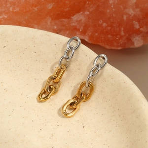 Detailopname van tweekleurige kettingoorbellen in goud en zilver op keramiek en zout