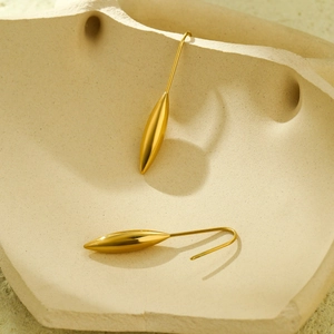 Vue détaillée des boucles d'oreilles dorées polies posées sur un plateau en céramique
