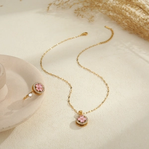 Set collana e anello d'oro con quadrifoglio rosa e zirconi su una superficie di pietra