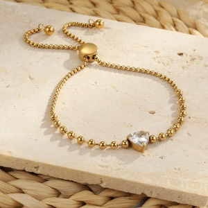 Adjustable gold stainless steel heart zircon bracelet on a warm textured stone background