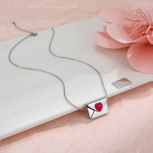 Detailansicht der silbernen Briefumschlag-Halskette mit rotem Herz auf rosa Krepppapier