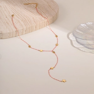 Detalle de collar en Y con estrellas doradas y cuentas rosas sobre piedra mármol