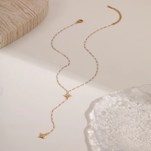 Detalle de collar en Y dorado con colgantes de estrella y cuentas blancas redondas