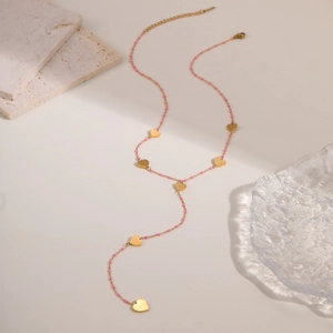 Detalle de collar lariat en Y dorado con cuentas rosas y colgantes de corazón
