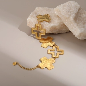 Detail eines 18k Gold Kreuzarmbands mit Hammerschlag-Textur auf weißem Naturstein