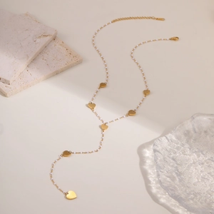 Primer plano de collar en Y dorado con colgantes de corazón, cuentas blancas y cierre de mosquetón