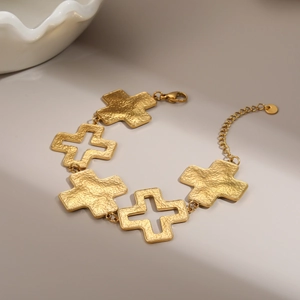 Detail eines 18k Gold-Kreuzarmbands mit gehämmerter Metallstruktur und praktischem Karabiner