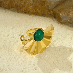 Macro detail van gouden waaiervormige ring met groene natuursteen op zand