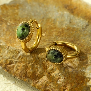 Gouden oorbellen met groene natuursteen op steenoppervlak voor een vintage esthetiek