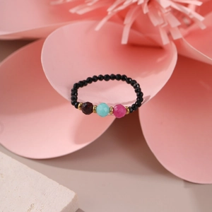 Macro detail of elastic beaded ring with natural black beads and three colored stones