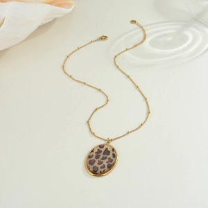 Collana vintage dorata con ciondolo a macchia di leopardo e catena a sfere su sfondo chic