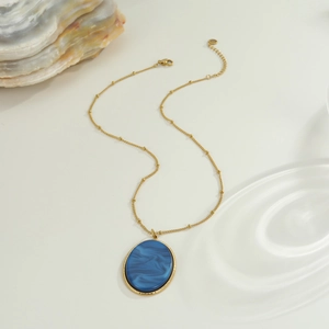 Dettaglio della collana dorata a perline con pendente ovale blu marmo e riflessi d'acqua