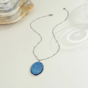 Dettaglio collana a catena argentata con ciondolo ovale in resina blu e effetto mare