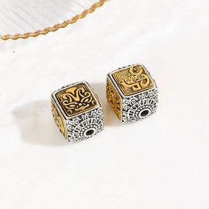 Macro shot of two square vintage alloy beads with intricate beast carvings and double-tone finish