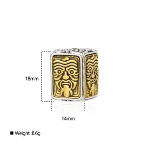 Macro shot of ethnic silver alloy square bead with mask relief and gold details