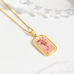 Close-up of golden necklace with pink enamel rectangle pendant featuring a red seahorse
