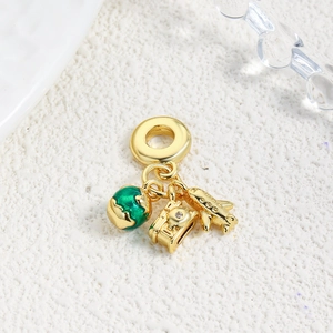 Macro shot of gold travel charms featuring green enamel globe, camera, and airplane