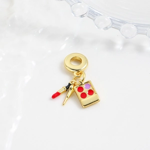 Macro detail of gold makeup charms featuring lipstick, brush, and eye shadow for bracelets