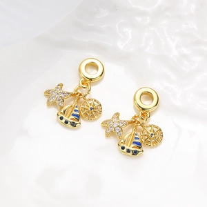 Detailed close-up of gold nautical charms with starfish, sailboat, and rudder on white stone