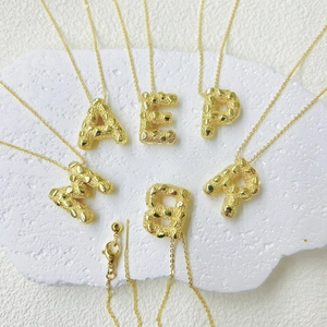 Detail van 18k gouden letterhangers met hart-hamerslagtextuur en verstelbare karabijnsluiting