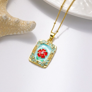 Détail macro du pendentif en or vintage avec rose rouge et goutte d'huile bleue sur blanc