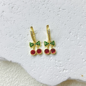 Pendientes de cereza con gemas rojas y acabado dorado sobre fondo de mármol blanco