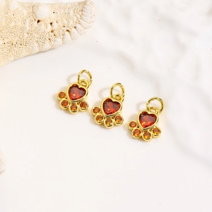 Close-up of three gold paw pendants with red heart stones on white textured background