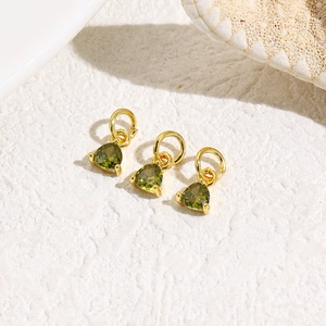 Detailed view of three gold triangle charms with green pear-cut zircon on white rock