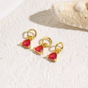 Three gold triangle pendants with red zircon stones on a white stone background