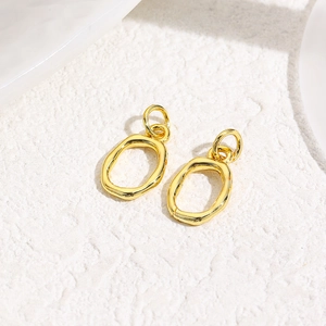 Detailed view of handmade textured gold-plated oval heart charms on a white stone background