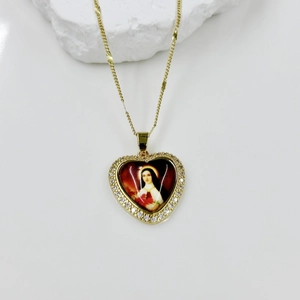 Macro detail of heart-shaped gold pendant featuring red enamel Virgin Mary and zircon border