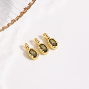 Detailed view of three oval gold-plated charms with emerald green zircons for jewelry making
