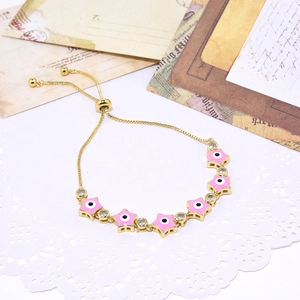Close-up of golden adjustable bracelet with pink enamel stars and zircon evil eye details