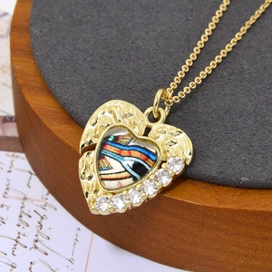Detail van een gouden hartvormige hanger met regenbooginlay en zirkoon aan een ketting