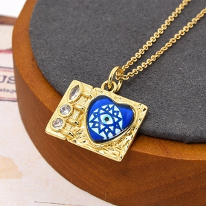Macro-opname van gouden boekvormige hanger met blauw boze oog hart en zirkonia's
