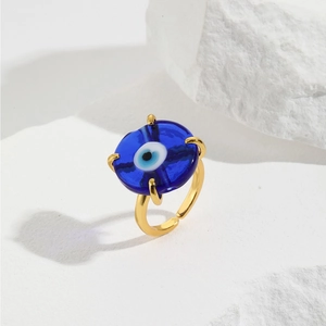 Adjustable gold evil eye ring with blue glass charm on white aesthetic background