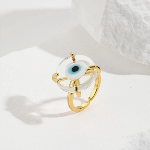 Macro shot of gold plated evil eye open ring on white stone background texture
