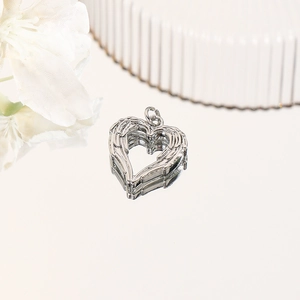 Polished silver heart pendant with textured angel wings on a mirror reflective surface