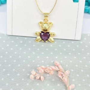 Close-up of golden teddy bear pendant with a purple heart-shaped zircon on a fine chain