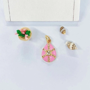 Detailed macro view of pink enamel teardrop pendant with gold cross patterns and zircons