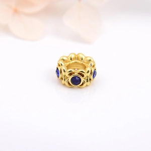 Macro shot of gold-plated hollow bead with blue stones on a reflective surface