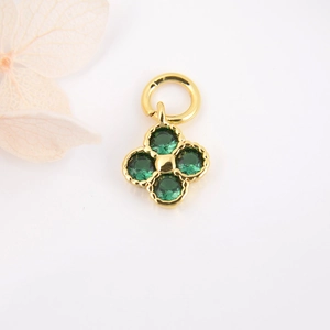 Detailed view of a gold clover charm with four green zircons and beaded edge craftsmanship
