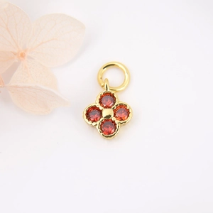 Detailed macro view of a gold four-leaf clover pendant with red zircon stones on white background