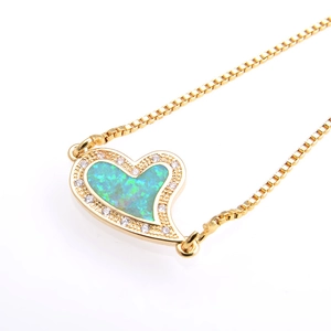 Macro detail of gold-plated heart pendant with blue-green opal and sparkling zircons