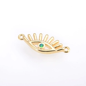 Close-up of gold-plated evil eye connector with green gemstone and eyelash detail