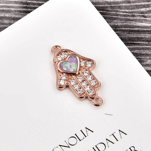 Makroaufnahme von Hamsa-Verbinder aus Roségold mit Herz-Opal und Zirkon-Besatz