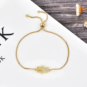 Detalle de pulsera de mano de Hamsa dorada con pedrería blanca e incrustación de ópalo