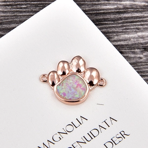 Pendentif patte en or rose avec opale rose et anneaux latéraux sur fond de bois sombre